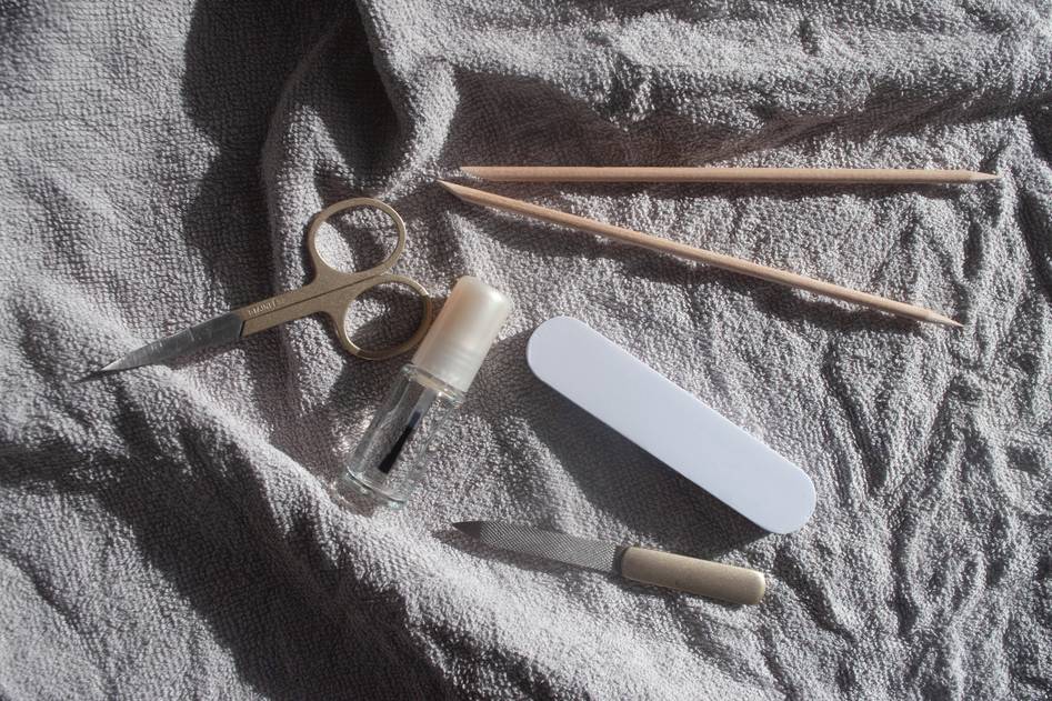 A close-up of nail buffing tools and polished nails on a soft pink background